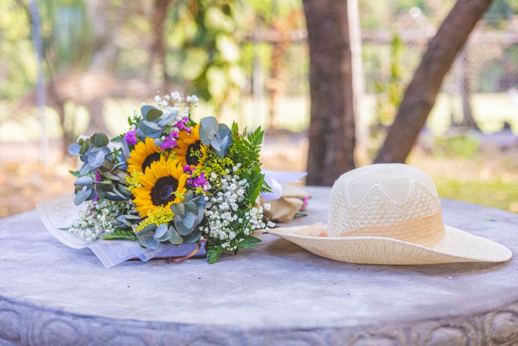 Vibrant sunflower bouquet with straw hat on a stone table in a sunny park setting.